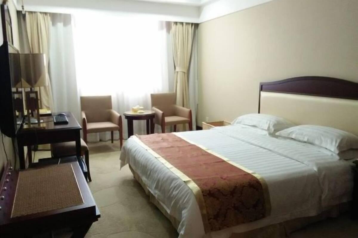 Ein Hotelzimmer mit einem Bett, einem Schreibtisch, einem Sessel, einem kleinen Tisch und Vorhängen.