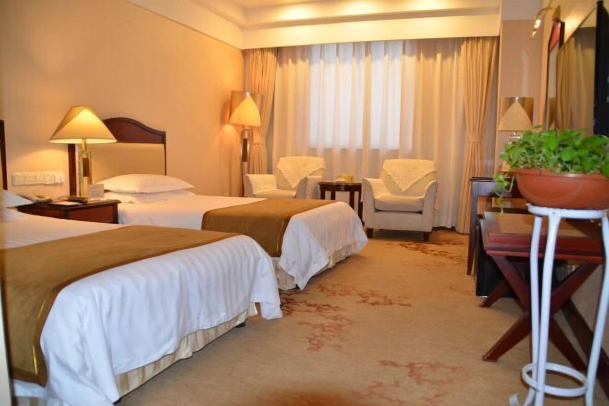 Ein Hotelzimmer mit zwei Betten, einem Schreibtisch, einem Stuhl, einer Lampe und einer Topfpflanze.
