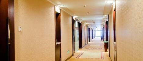 A hotel corridor with carpeted floors and doors on both sides leading to rooms.