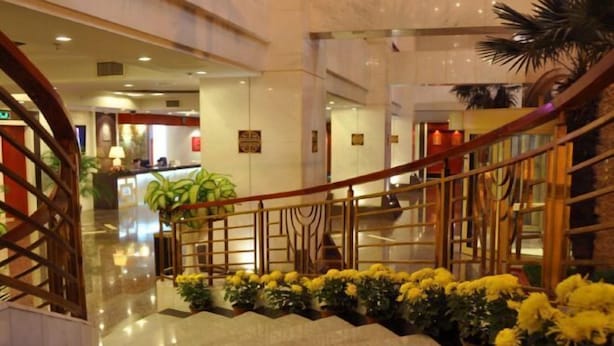 Eine Hotelhalle mit einer Marmortreppe, einer Rezeption und Blumentöpfen.