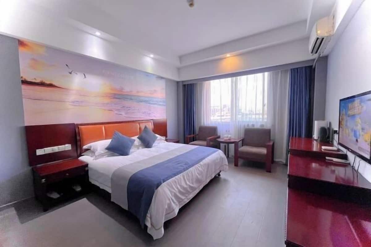 A hotel room with a large bed, a desk, a chair, and a television.
