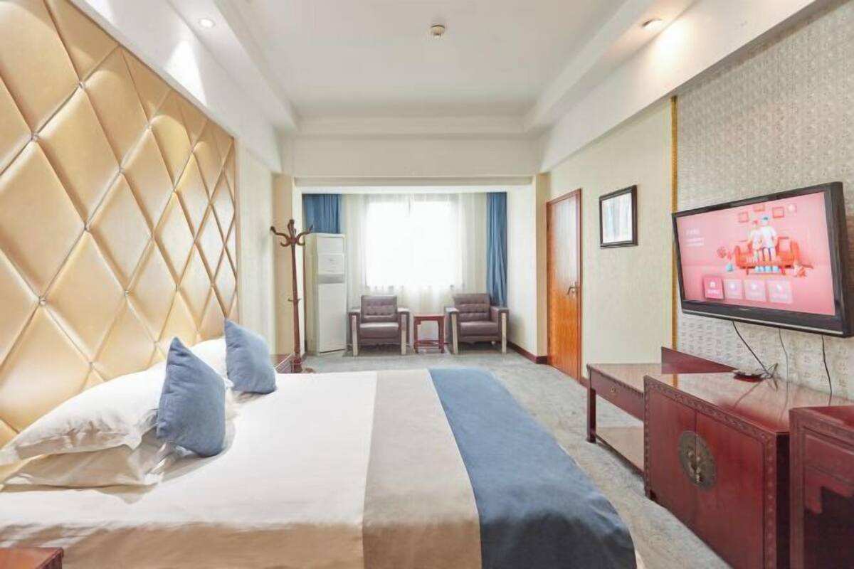 A hotel room with a large bed, a television, a desk, and a seating area with chairs.