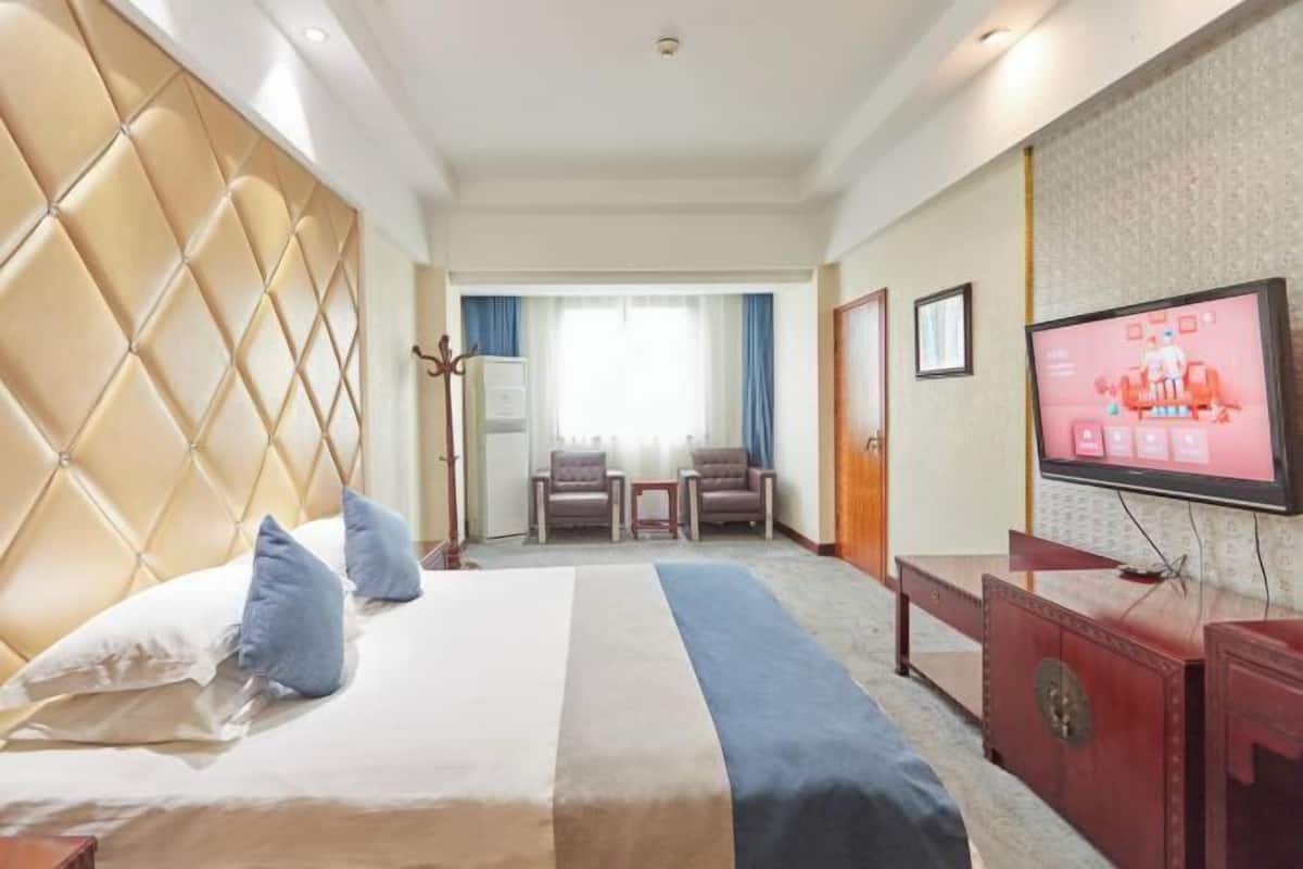 Quarto de hotel com uma cama grande, televisão, escrivaninha e área de estar com cadeiras.