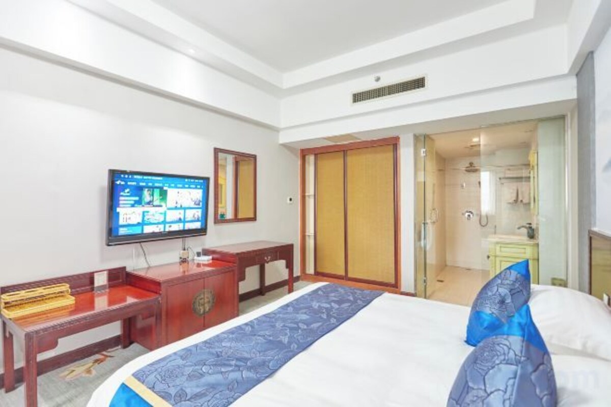 A hotel room with a bed, a desk, a television, and a bathroom visible through an open door.