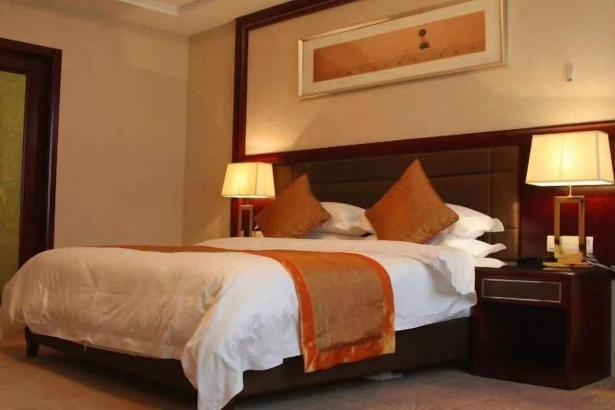 A hotel room with a large bed, two bedside tables with lamps, a framed picture on the wall, and a carpeted floor.