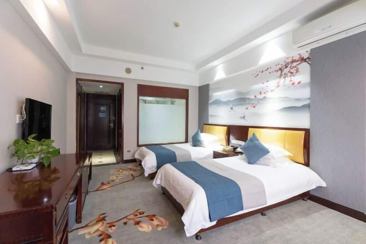 A hotel room with two beds, a desk, a TV, and a wall with a floral mural.