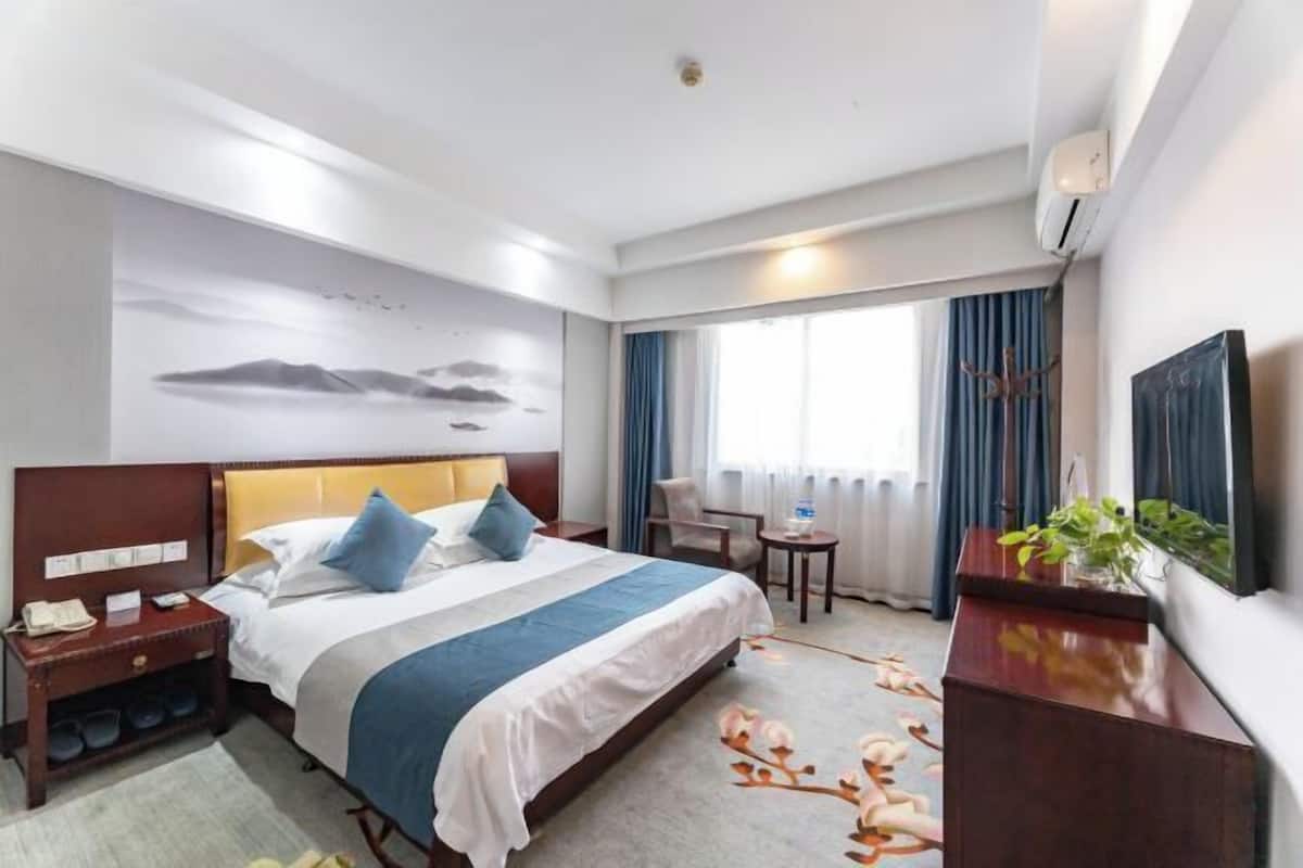 A hotel room with a bed, a desk, a chair, a TV, and a window with curtains.