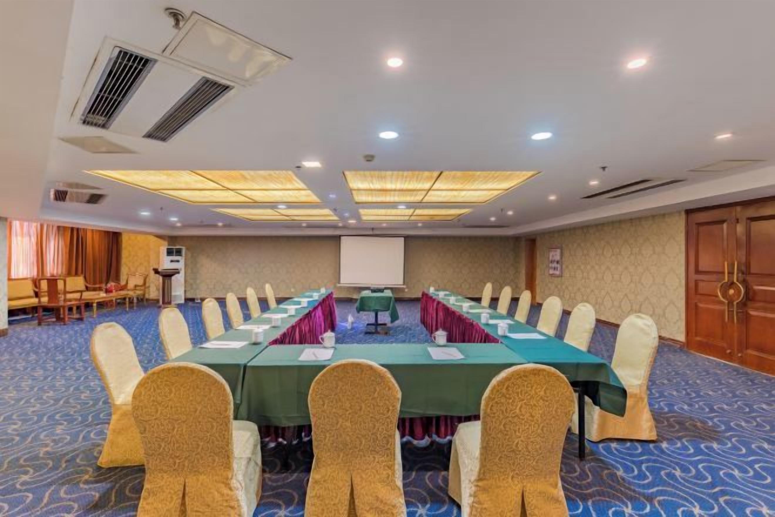 A conference room with a long table, chairs, a projector screen, and a carpeted floor.