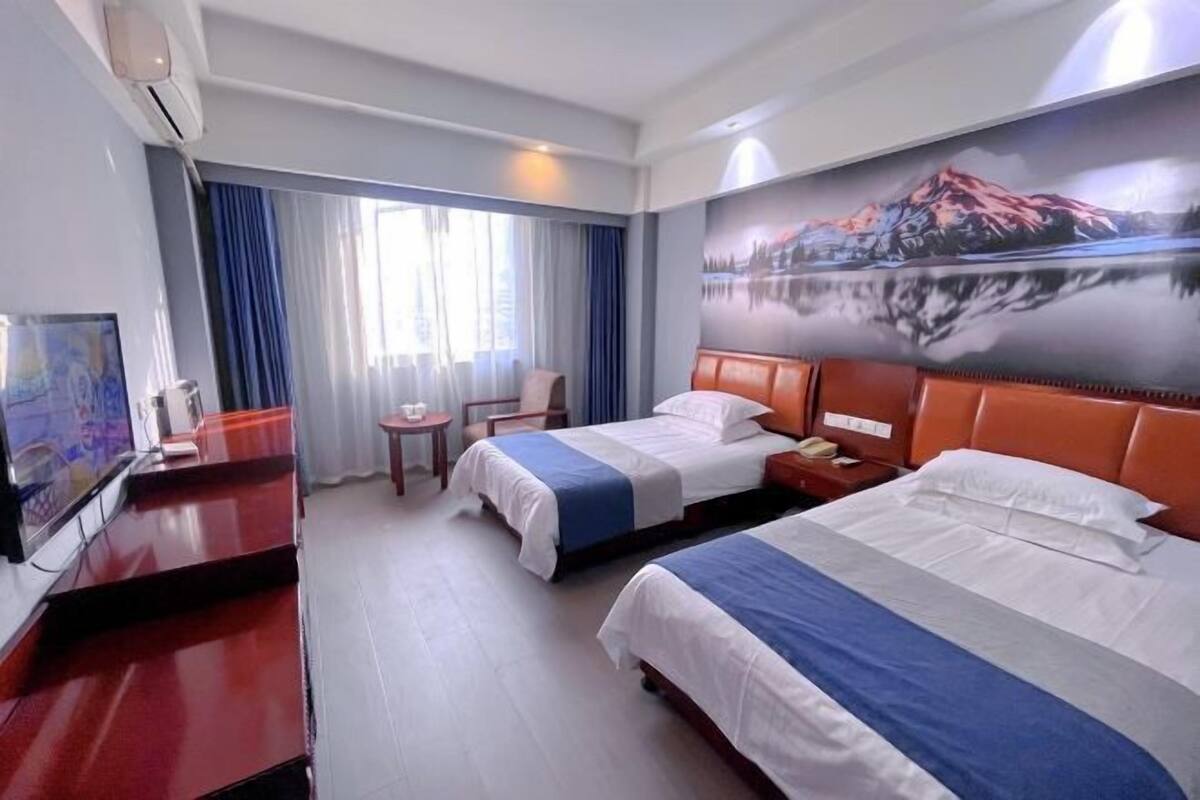 A hotel room with two beds, a desk, a chair, a TV, and a painting on the wall.