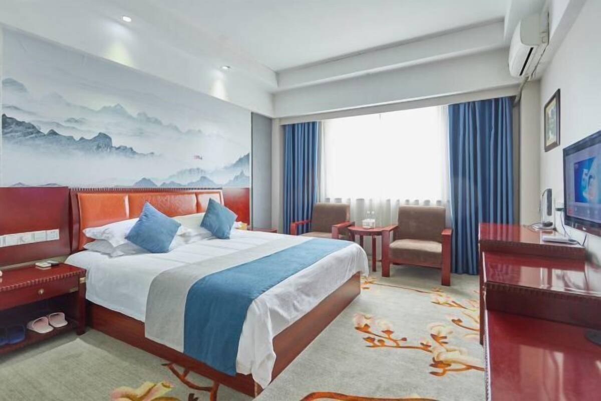 A hotel room with a bed, a desk, a chair, a TV, and a window with curtains.