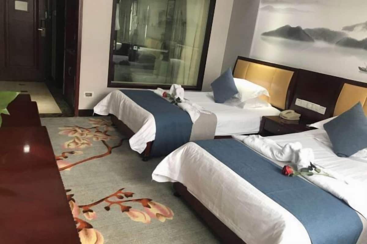 A hotel room with two beds, a wooden desk, and a large window.