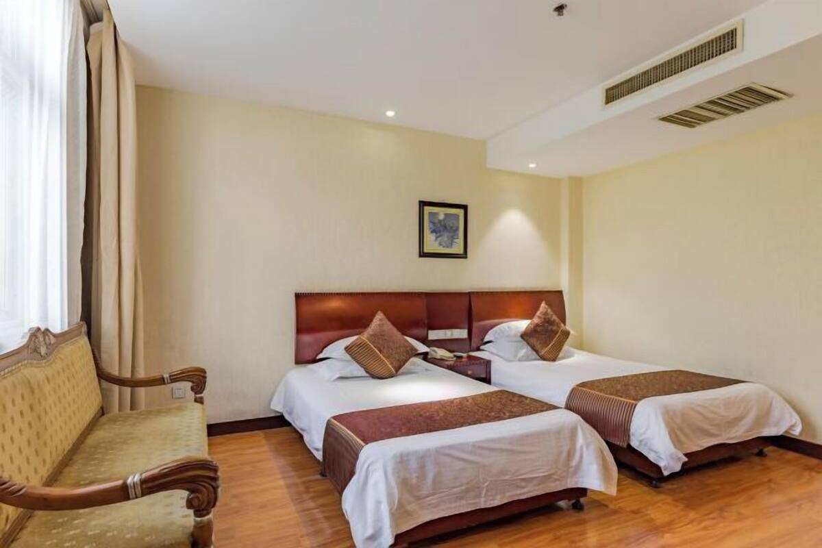 A hotel room with two beds, a wooden bench, and a framed picture on the wall.