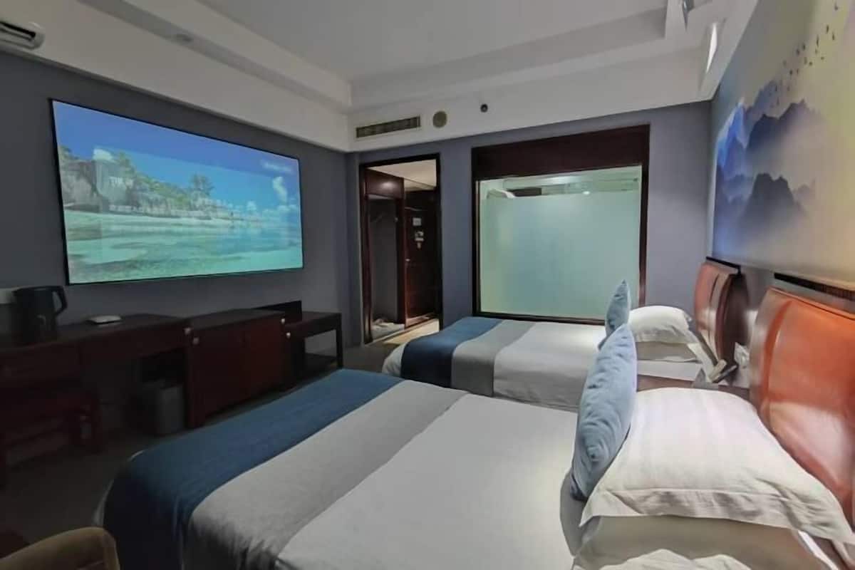 A hotel room with two beds, a desk, a TV, and a bathroom door.