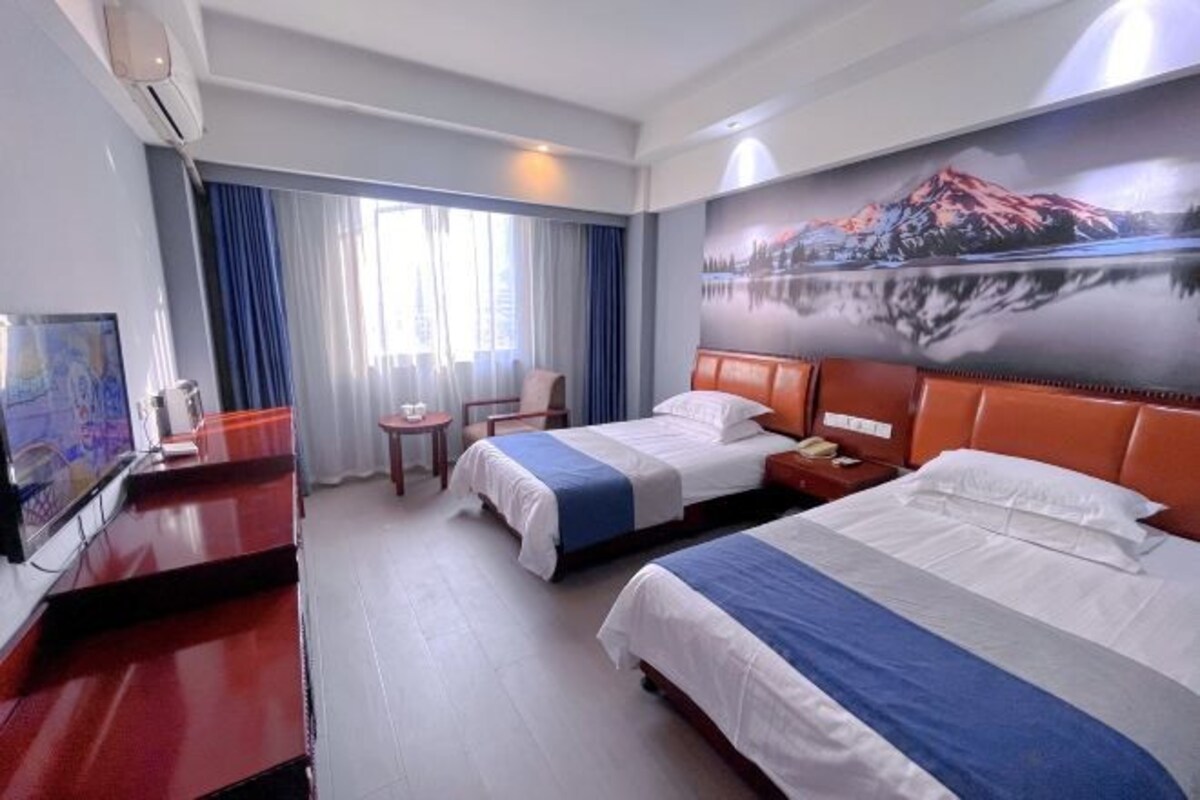 A hotel room with two beds, a desk, a chair, a TV, and a window with curtains.