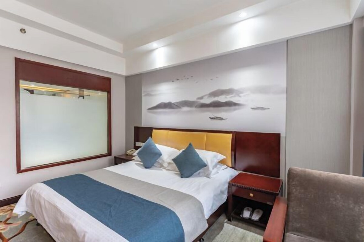 A hotel room with a bed, a nightstand, a chair, a wall-mounted TV, and a shoe rack.