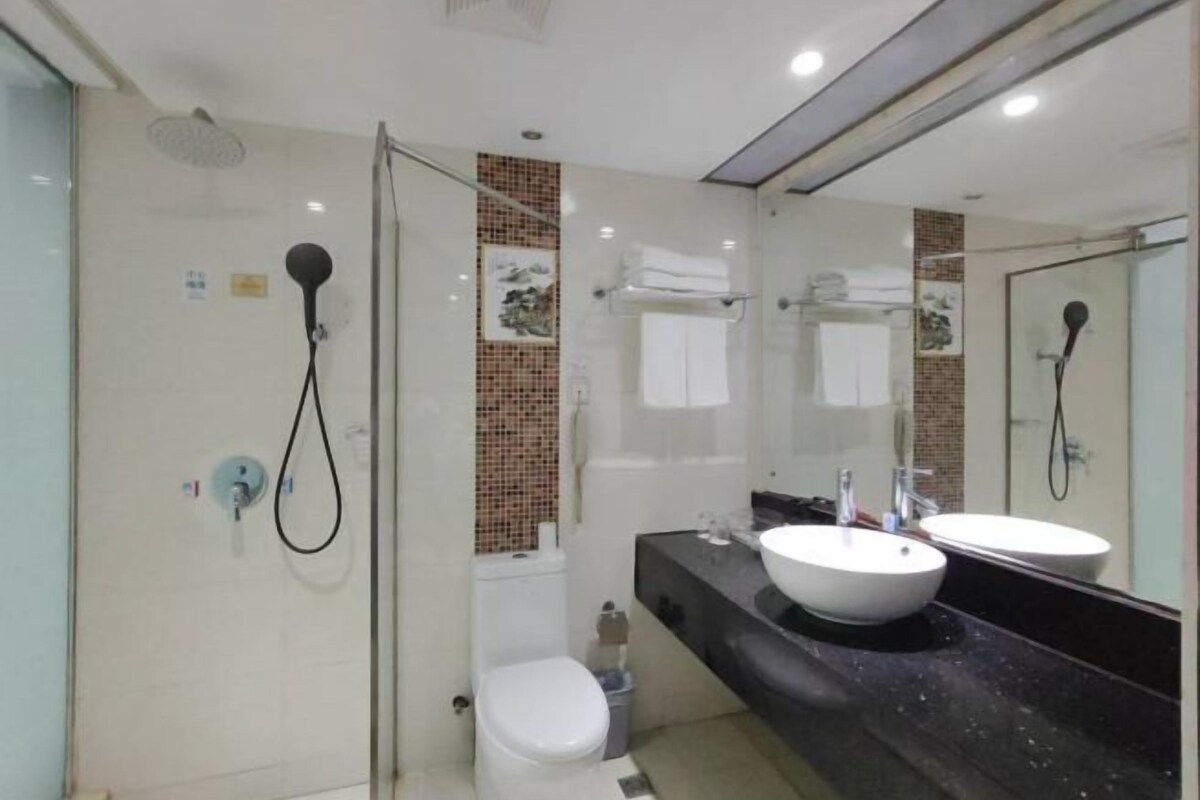 A modern bathroom with a glass-enclosed shower, a white toilet, a black countertop with a white sink, and a large mirror.