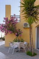 An outdoor seating area with a table and chairs, a palm tree, and a building with a yellow facade.