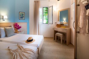 A hotel room with a bed, a vanity with a mirror, a window with curtains, and a door with towels. - Melissa Hotel (Faistos)