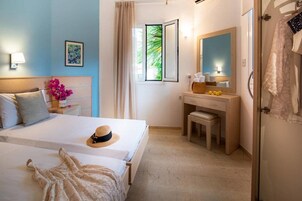A hotel room with a bed, a vanity with a mirror, a window with curtains, and a door with towels.