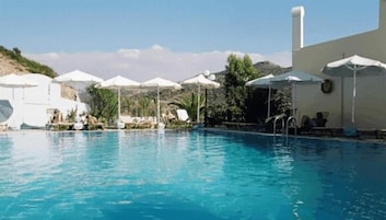 A swimming pool with lounge chairs and umbrellas, surrounded by a building with a white facade.