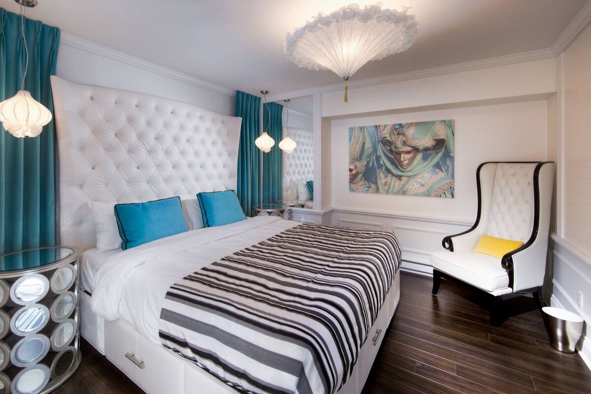 Un dormitorio amplio con una cama grande, cabecera capitonada, un chaise lounge y una lámpara decorativa en el techo.