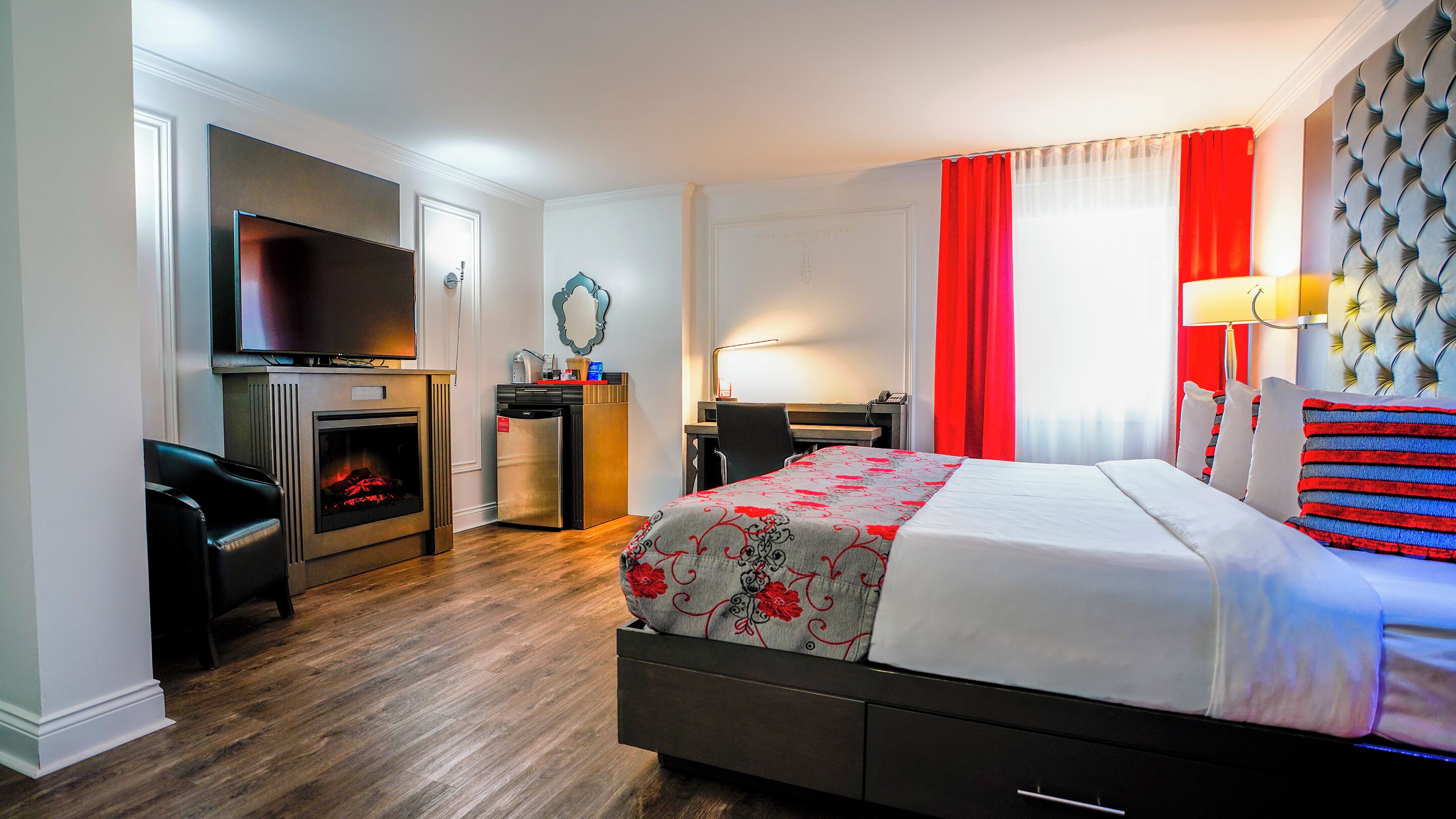 Habitación de hotel con cama, escritorio, silla, televisión, chimenea y ventana con cortinas.