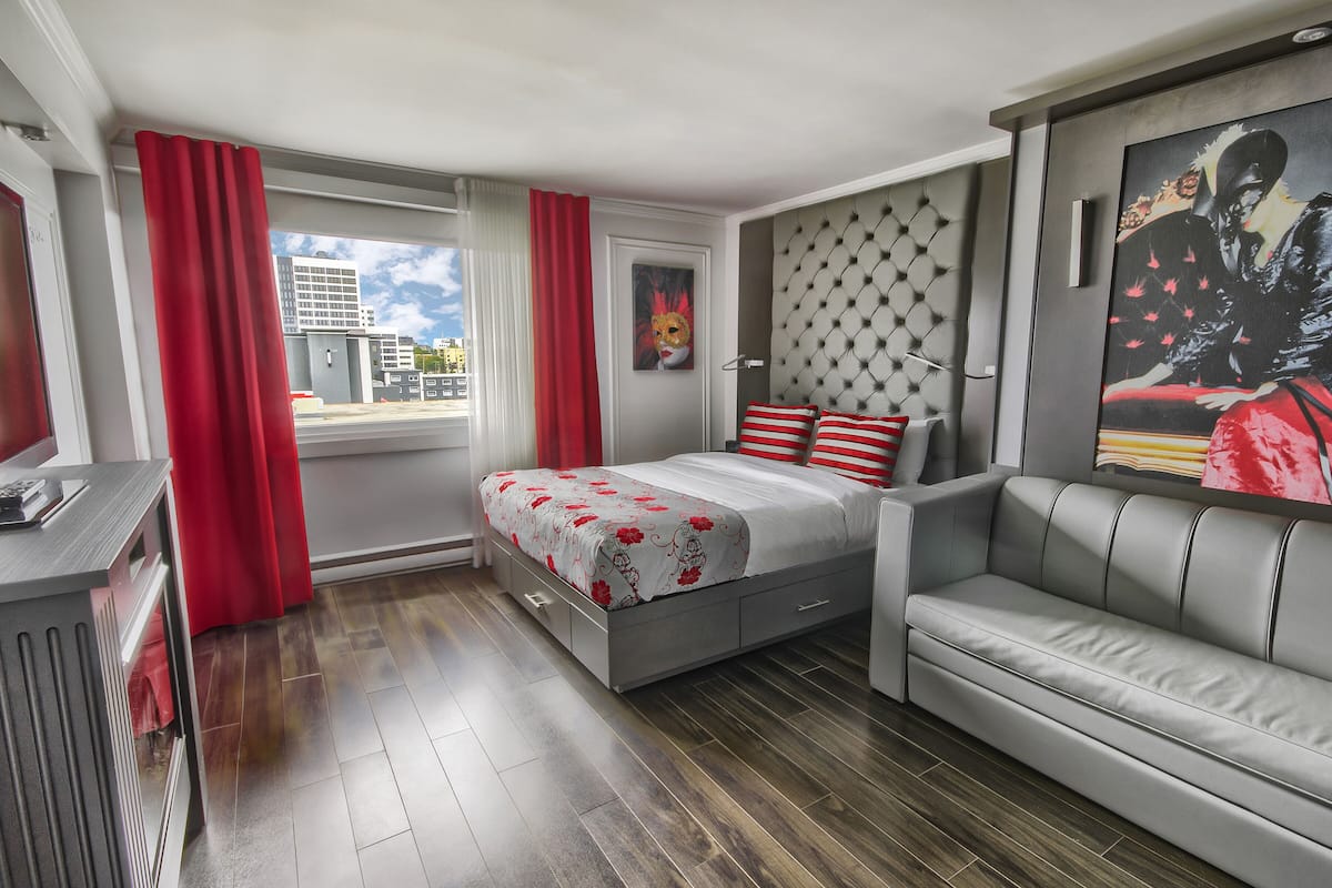 Un dormitorio moderno con cama, sofá, un cuadro y vistas a edificios.