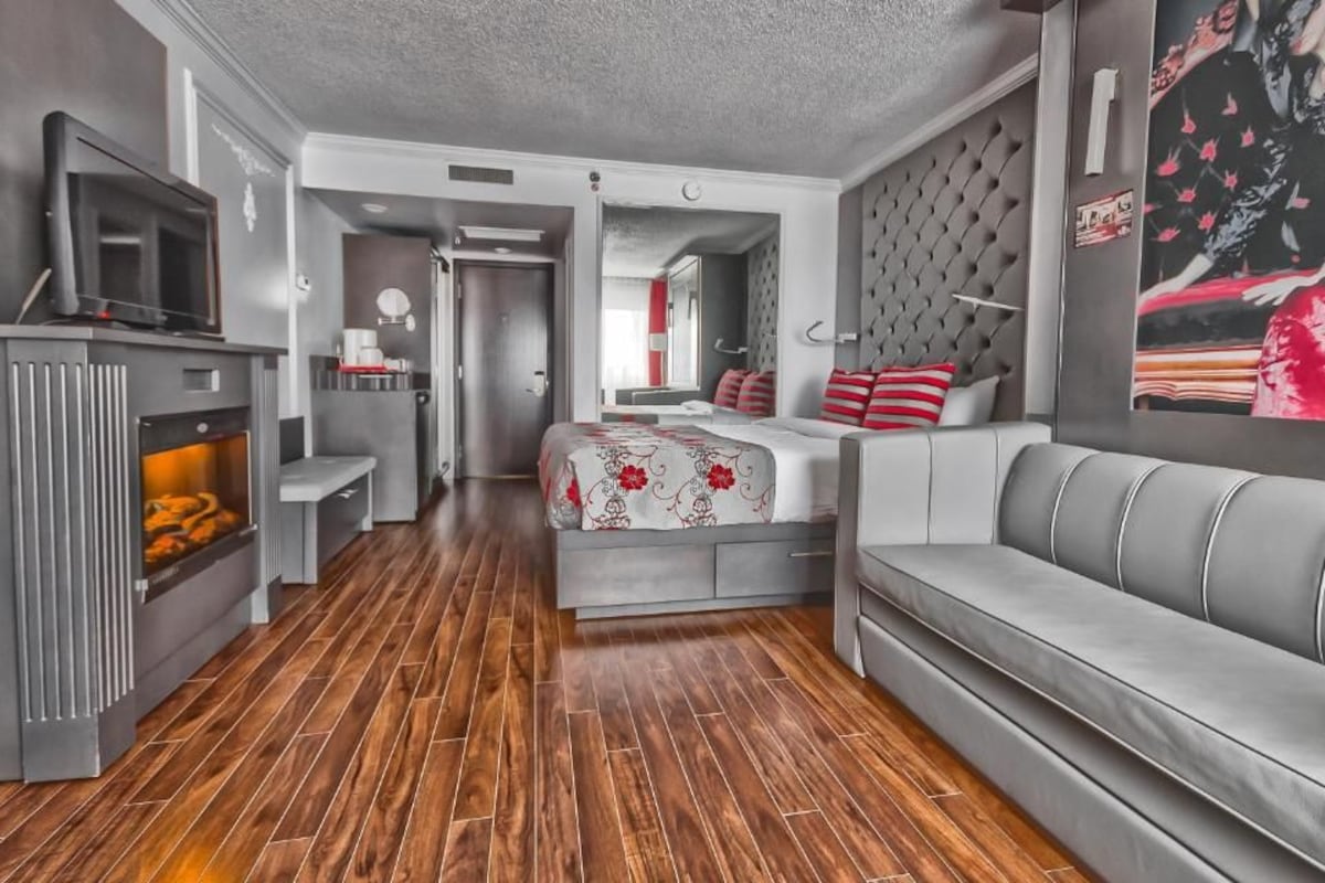 Une chambre d’hôtel moderne avec un canapé, un lit avec une literie rouge et blanche, une télévision et une cheminée.