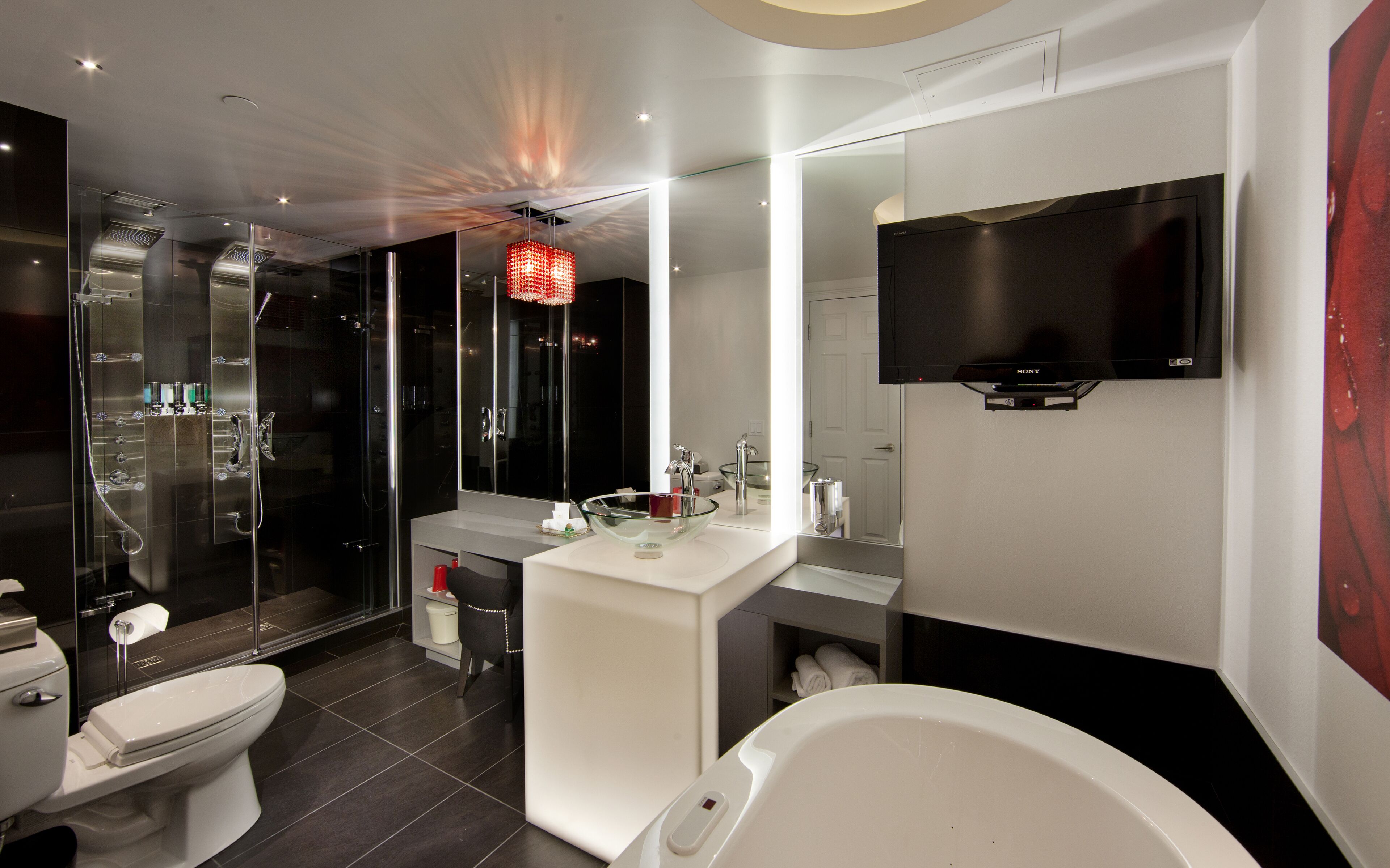 A modern bathroom with a glass-enclosed shower, a white sink with a large mirror, a toilet, and a bathtub.