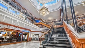 A grand hotel lobby with a central staircase, multiple floors, and a chandelier.