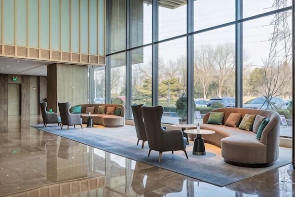 Eine geräumige Lobby mit einer großen Glaswand, einer Sitzecke mit Sofas und Sesseln und einem polierten Boden.