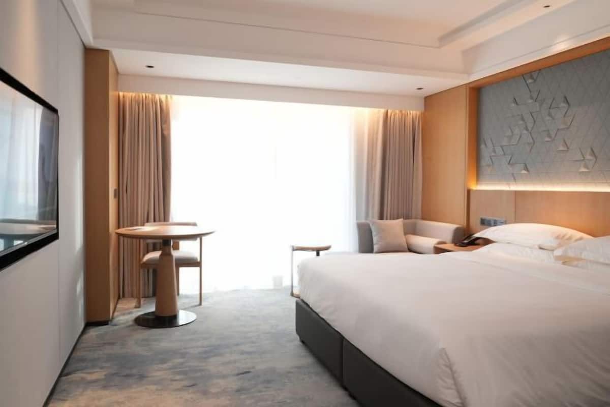 A hotel room with a bed, a round table, a chair, and a large window with curtains.