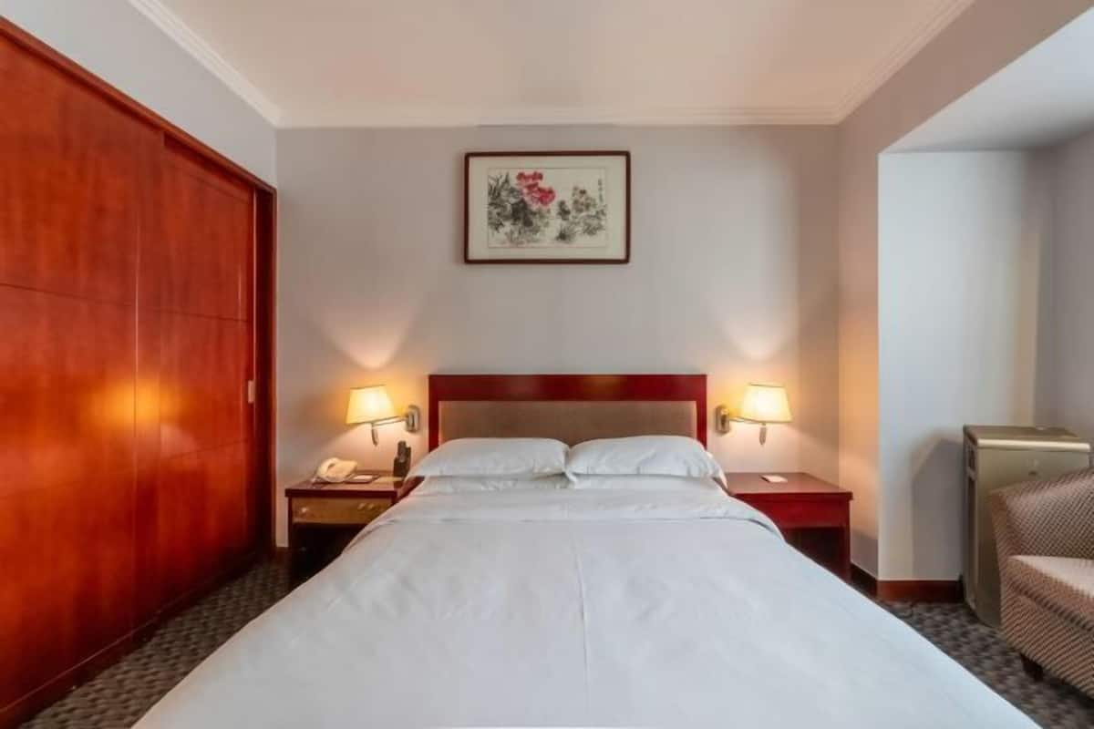 Ein Hotelzimmer mit einem großen Bett, zwei Nachttischlampen, einem Holzschrank, einem gerahmten Kunstwerk an der Wand und einem Sessel.