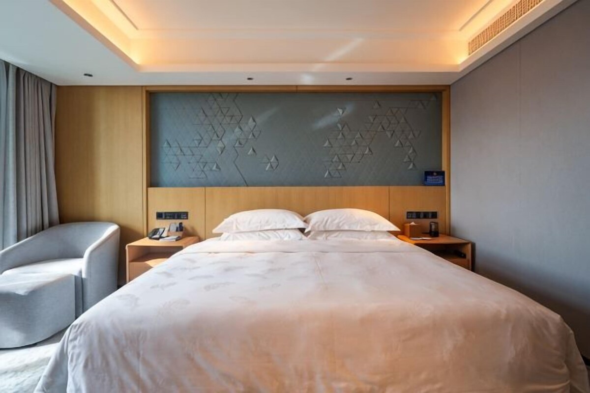 Une chambre d’hôtel avec un grand lit, deux tables de chevet, une chaise et un panneau décoratif mural.