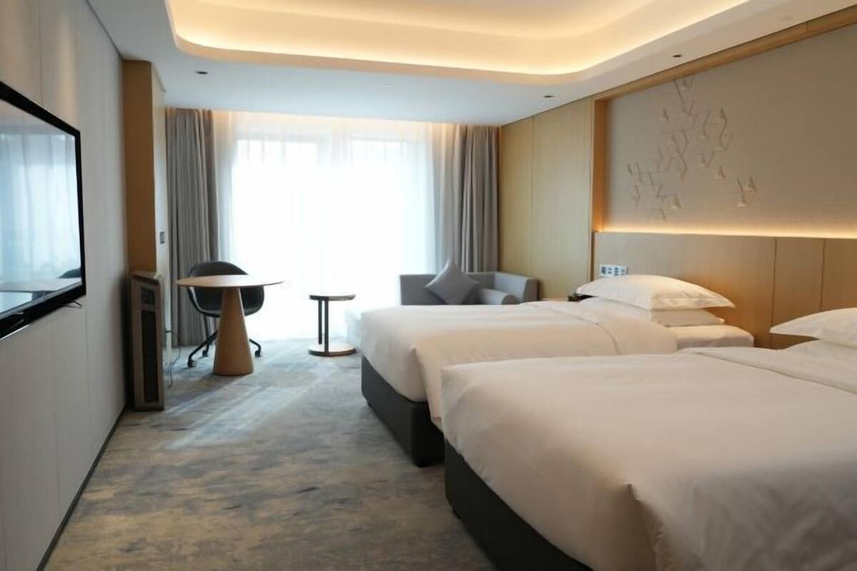 A hotel room with two beds, a desk, a chair, and a large window with curtains.