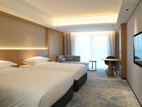 Ein Hotelzimmer mit zwei Betten, einem Schlafsofa, einem kleinen Tisch und einem Fernseher.