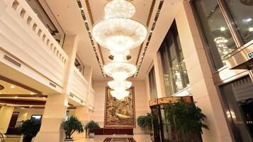 A hotel lobby with a central chandelier, large windows, and a reception desk.