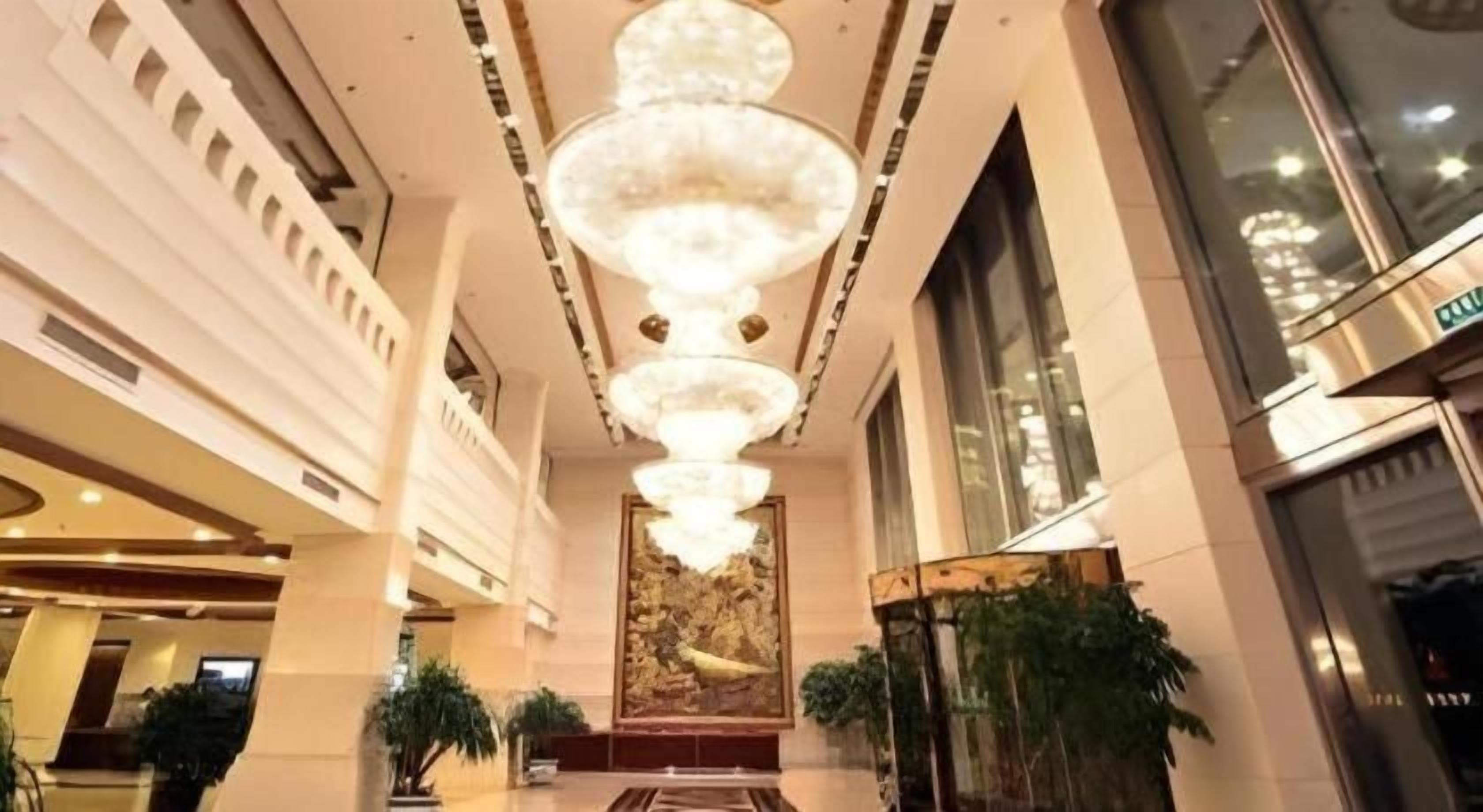 Un vestíbulo de hotel con una gran lámpara central, ventanas amplias y una recepción.