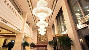 Un vestíbulo de hotel con una gran lámpara central, ventanas amplias y una recepción.