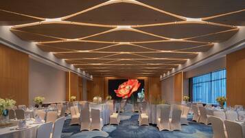 Un salón de conferencias con un diseño moderno de techo, una pantalla grande al frente y filas de mesas con sillas.