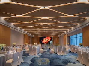 Une salle de conférence dotée d’un plafond au design moderne, d’un grand écran à l’avant et de rangées de tables accompagnées de chaises.