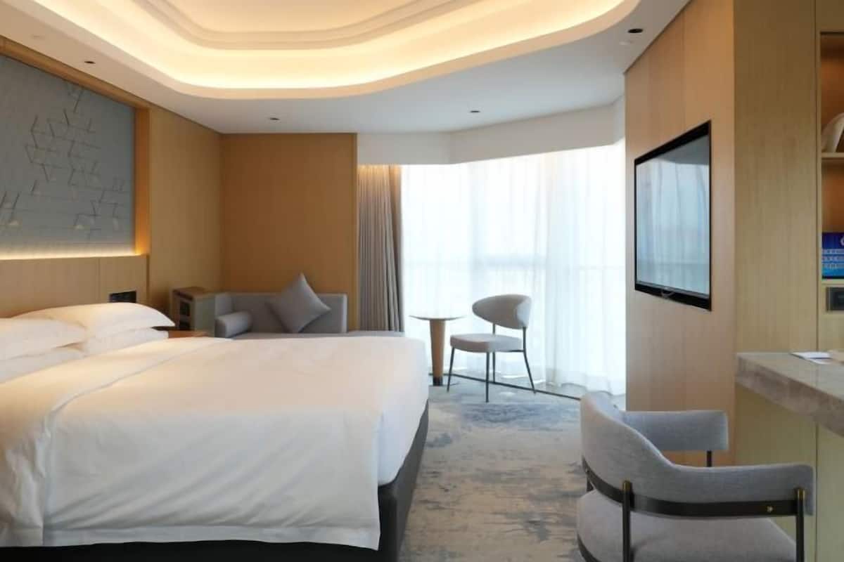 A hotel room with a large bed, a desk, a chair, a TV, and a window with curtains.