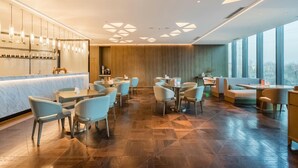 Un restaurant moderne doté d’un bar, de différents types de tables et de grandes fenêtres.