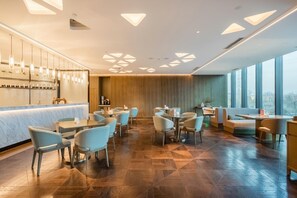 Un restaurant moderne doté d’un bar, de différents types de tables et de grandes fenêtres.