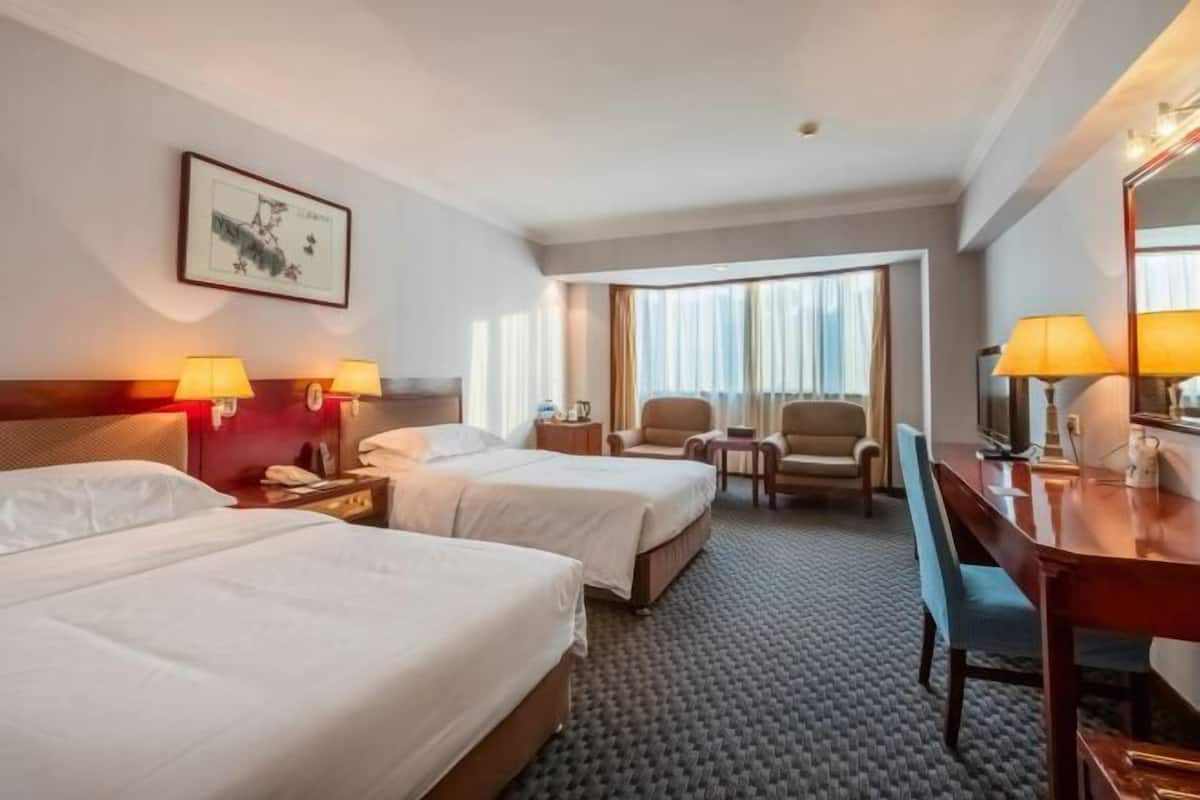 Ein Hotelzimmer mit zwei Betten, einem Schreibtisch, einem Stuhl und einem großen Fenster.