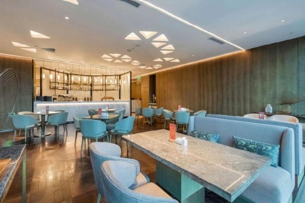 Um saguão de hotel moderno com área de bar, espaços de estar e uma parede de destaque em madeira.