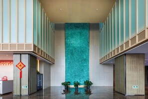 Un hall d’entrée spacieux agrémenté d’un grand panneau décoratif vertical, d’un comptoir de réception et de plantes en pot.