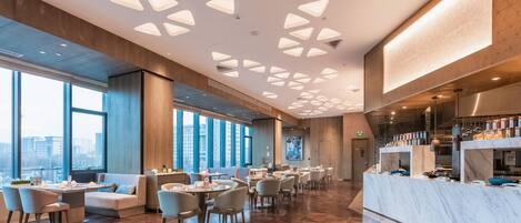 A modern restaurant with a high ceiling, large windows, and a marble counter.