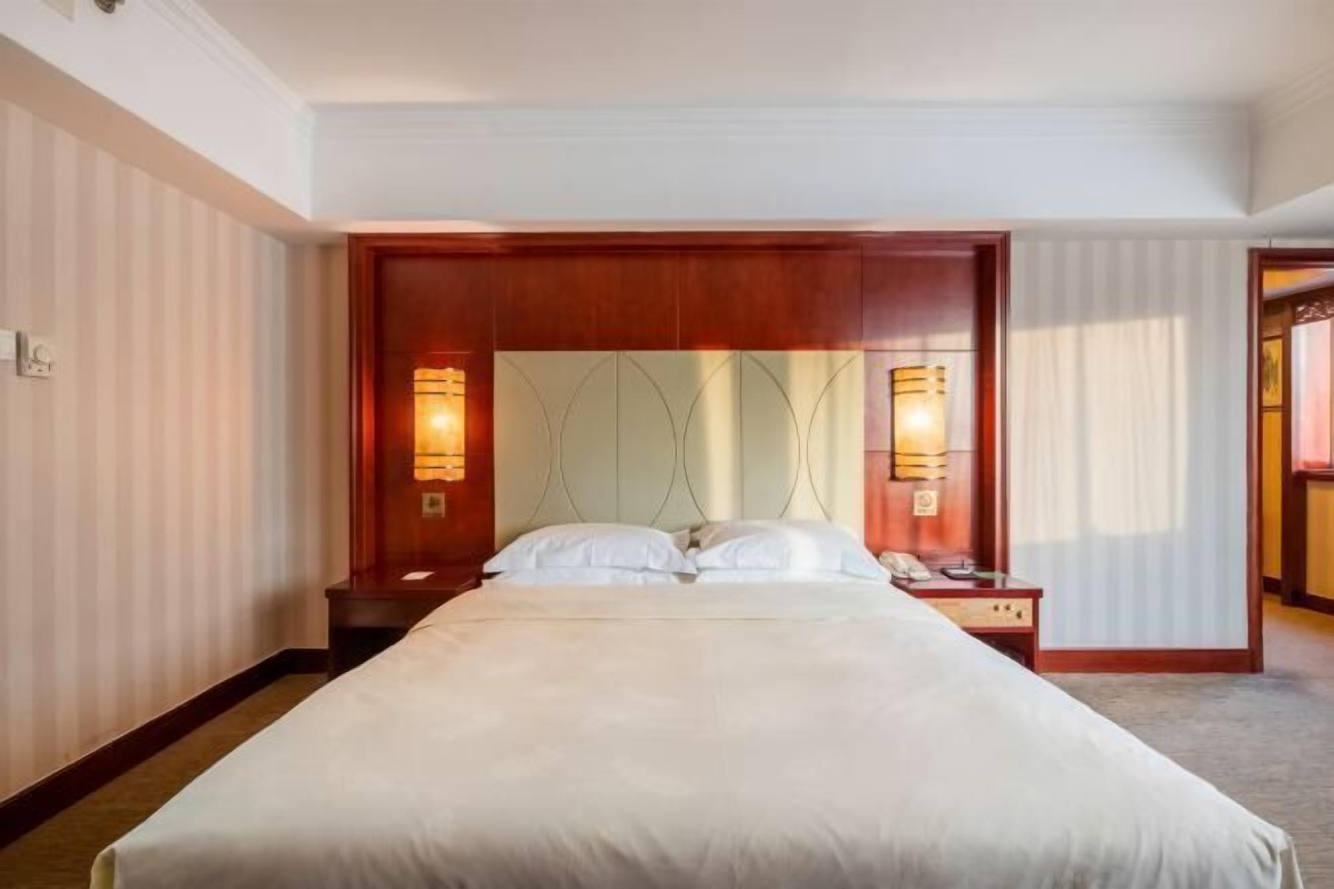 Ein Hotelzimmer mit einem großen Bett, einem Holz-Kopfteil, zwei Nachttischen mit Lampen und einem Spiegel über dem Bett.