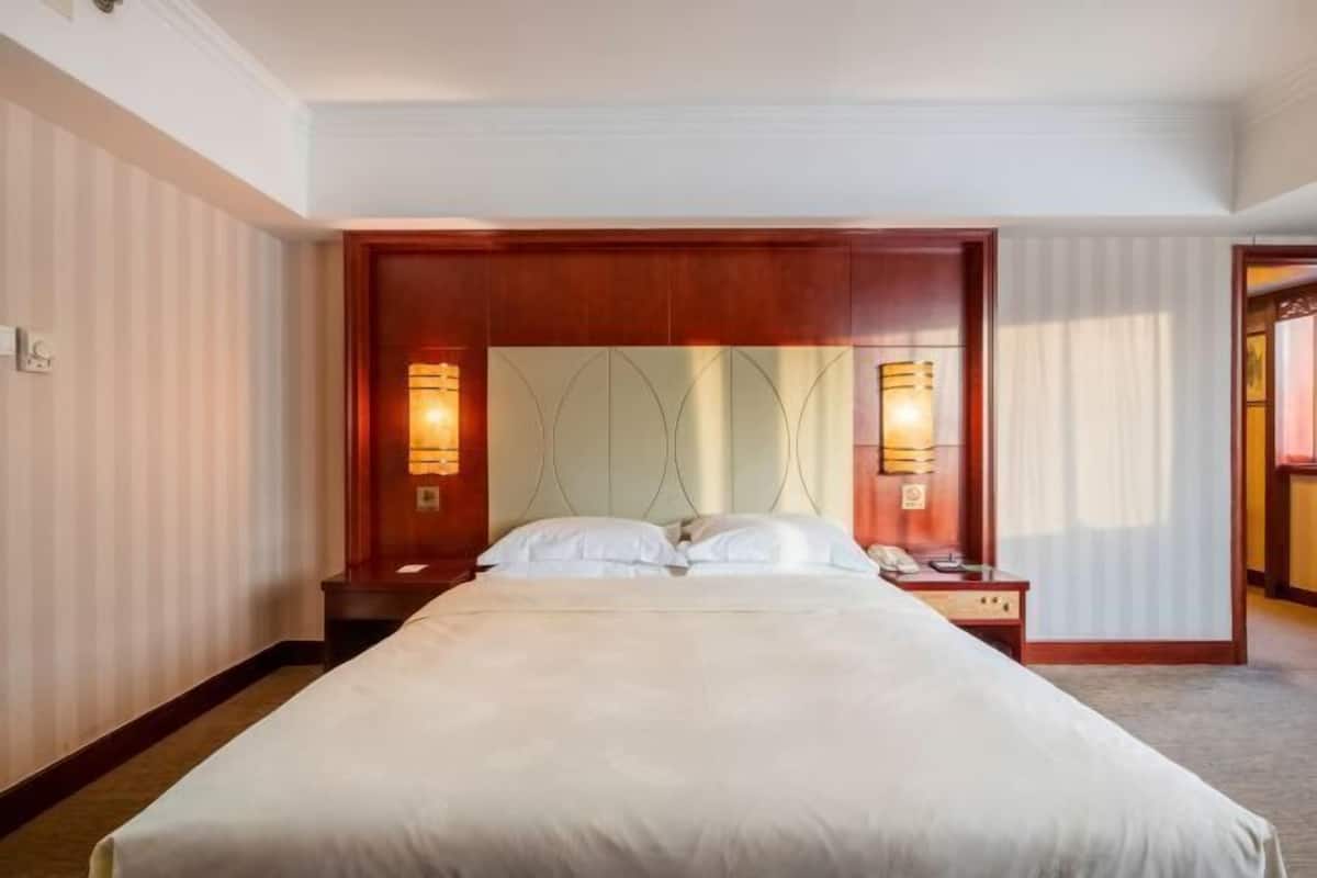 Ein Hotelzimmer mit einem großen Bett, einem Holz-Kopfteil, zwei Nachttischen mit Lampen und einem Spiegel über dem Bett.